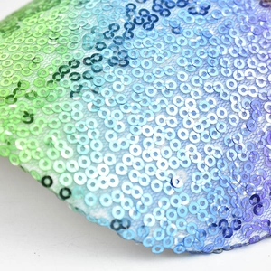 Macro view of gradient sequins on mesh fabric showing vibrant purple to green transition