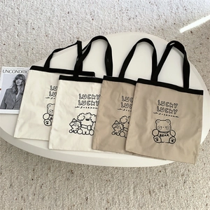 Close-up of durable canvas tote bags with black straps and cute bear embroidery details