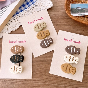 Three cute fish-shaped cartoon hair clips in beige and brown tones on a wooden table