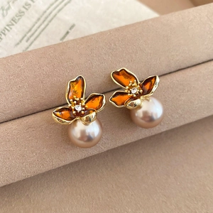 Macro detail of French retro flower earrings with orange enamel and round pearls