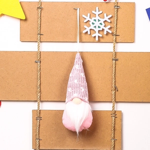 Pink knitted Christmas gnome ornament with white polka dots hanging on rustic display