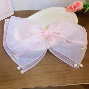 Detailed view of pink mesh bow hair clip with hanging pearl tassels on a wooden surface