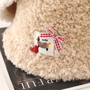 Détail d'un chapeau bob en sherpa beige avec écusson chiot et nœud rouge