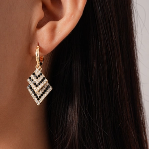 Macro view of gold geometric rhombus earrings with black and white pavé stones