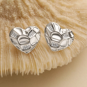 Silver heart stud earrings with stone wall texture and zircon on coral background