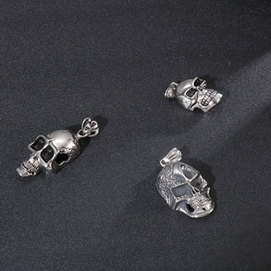 Three punk style silver skull pendants made of stainless steel on a dark textured background