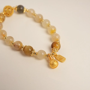 Vue macro de la breloque Fortune dorée et cloche sur bracelet en perles citrine
