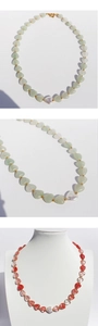 Detail of heart-shaped natural stone beaded necklace with baroque pearl on a white stand