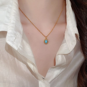 Close-up of a gold necklace featuring an oval turquoise pendant on a female model