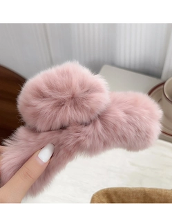 Detailed view of a soft pink faux fur hair claw clip held by a hand in natural light