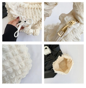 Detail of white textured puff shoulder bag showing gold zipper and ruched fabric finish