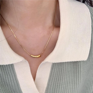 Close-up of minimalist gold curved tube pendant necklace on a knit polo shirt