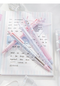 Close-up of pink and white retractable gel pens with ribbon bow design on open notebook