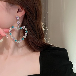 Gros plan de grandes boucles d'oreilles cœur argentées avec zircons colorés sur un modèle