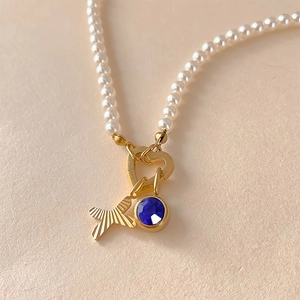 Gros plan détaillé d'un collier de perles avec lettre X gravée et pendentif en cristal bleu