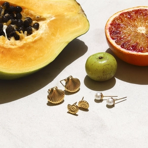 Detailed set of gold shell earrings and pearl studs on natural fruit backdrop