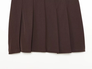Détail de l'ourlet de la jupe plissée marron foncé montrant la texture et le plissage