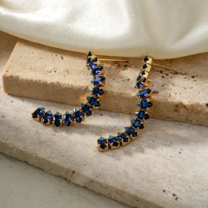 Macro shot of gold curved earrings with dark blue marquise cut stones on stone surface