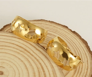 Détail de boucles d'oreilles étoile évidées en or 18K posées sur un support en bois