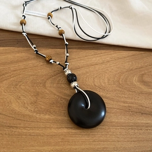 Close-up of black donut pendant with woven cord and decorative wood beads on wood