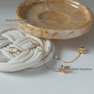 Detailed view of gold clover stud earring with pearl tassel and chain ear cuff