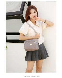 Detail of grey nylon crossbody bag with multi-layer zippers on beige shirt outfit