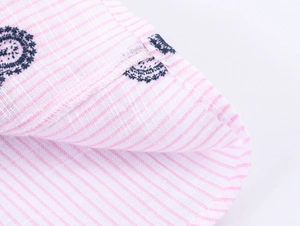 Détail du tissu à rayures roses avec broderie bleu foncé délicate et coutures fines