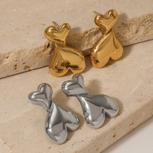 Polished double heart-shaped earrings in gold and silver finish on a stone background