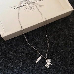 Macro detail of silver horse pendant and Lucky tag on a minimalist sweater chain