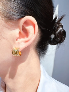 Close-up of a wide polished gold C-shape hoop earring worn on a model's ear