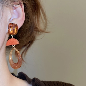 Close-up of geometric resin drop earrings featuring amber patterns and orange layered detail