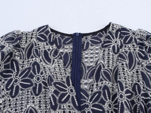 Detail des V-Ausschnitts mit weißer Stickerei und Lochspitze auf einem dunkelblauen Kleid