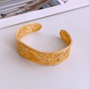 Macro detail of gold-plated open cuff bracelet featuring vintage relief pattern and texture