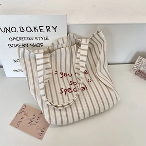 Detail of striped canvas tote bag with red embroidered slogan on white wooden background