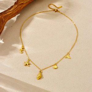 Gold chain necklace featuring starfish and seahorse pendants on a beach sand background