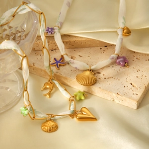 Détail du collier foulard en soie avec pendentifs coquillage doré, étoile de mer et cœur