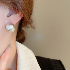 Close-up of matte silver C-shaped brushed metal earrings worn on a female model