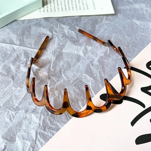 Detailed view of an amber tortoiseshell wavy headband on a textured gray background