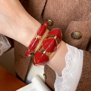 Detail of red enamel and gold vintage bracelets on a retro suit jacket sleeve