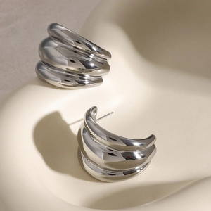 Detail of silver mirrored chunky earrings with multi-layered wave design on display stand