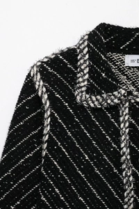 Close-up of black tweed jacket featuring a lapel collar with woven ribbon trim and frayed edges