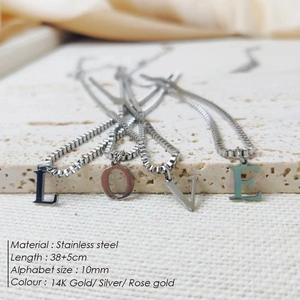 Close-up showing stainless steel LOVE letter pendant necklaces on a textured stone