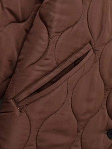 Detailed view of the dark brown quilted jacket featuring sleek wavy stitching and side pocket