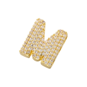 Macro shot of gold-plated letter M pendant fully iced with sparkling zirconia stones