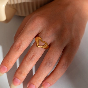 Close-up of heart-shaped hollow ring in gold finish worn by model on index finger