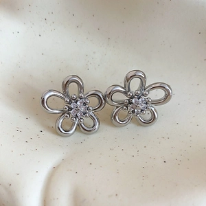 Macro detail of silver flower earrings with zircon center on ceramic tray