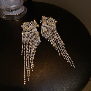 Detailed view of silver tassel earrings with sparkling crystals on black background