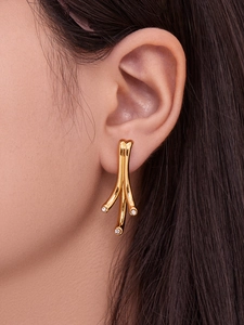 Vue macro de boucles d'oreilles branche dorée géométrique avec zircons sur un modèle