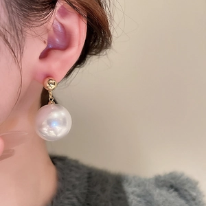 Close-up of model wearing gold-plated spherical stud earrings with large drop pearls