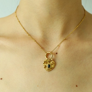 Detail of an 18K gold plated heart pendant necklace with a black teardrop gemstone